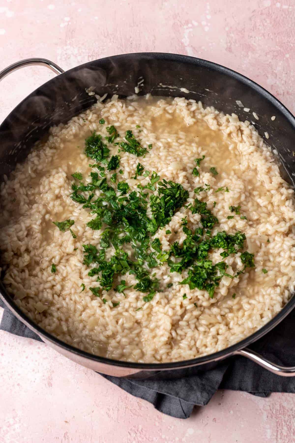 Parsley added to the almost fully cooked risotto in a large skillet.