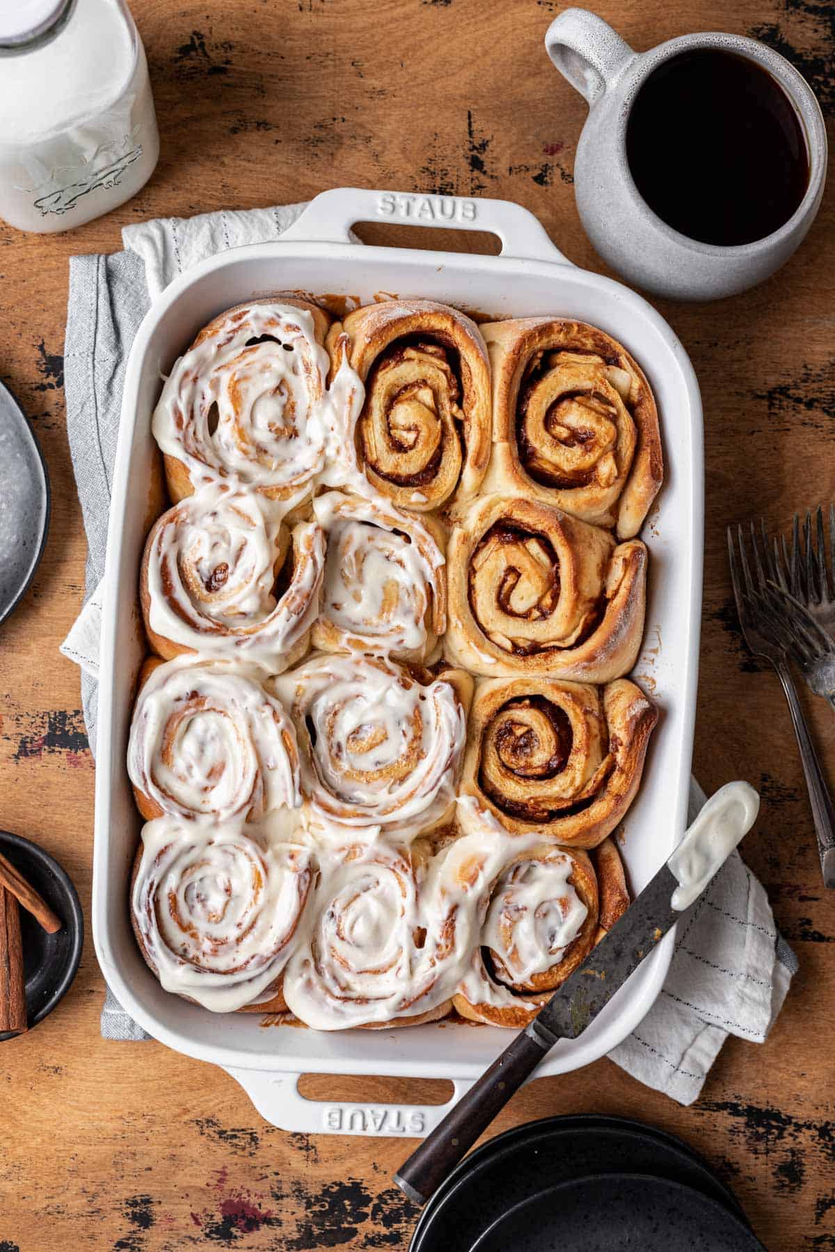 Cinnamon rolls with apple pie filling in a white baking dish topped halfway with cream cheese icing.