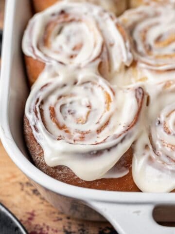 Cinnamon rolls with apple pie filling topped with a cream cheese icing in a baking dish.