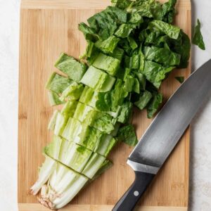 Romaine lettuce cut on a wooden cutting board with a chef's knife next to it.