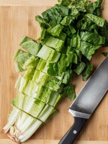 Romaine lettuce cut on a wooden cutting board with a chef's knife next to it.