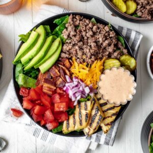 Loaded burger bowls topped with avocado, grilled pineapple, pickles, cheese, bacon, and tomatoes.