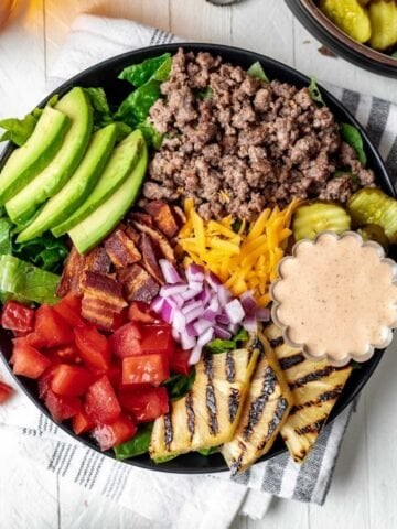 Loaded burger bowls topped with avocado, grilled pineapple, pickles, cheese, bacon, and tomatoes.