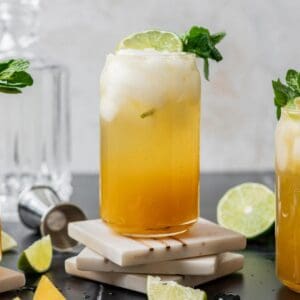 Mango mojito garnished with a lime slice and mint on top of white coasters.