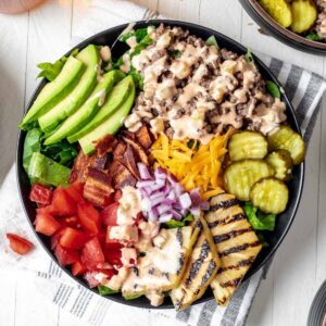 Loaded burger bowls topped with avocado, grilled pineapple, pickles, cheese, bacon, and tomatoes.