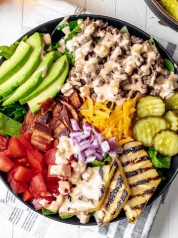 Loaded burger bowls topped with avocado, grilled pineapple, pickles, cheese, bacon, and tomatoes.