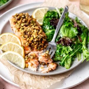 Pistachio crusted salmon on a plate with a side salad and a fork.