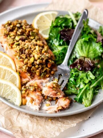 Pistachio crusted salmon on a plate with a side salad and a fork.