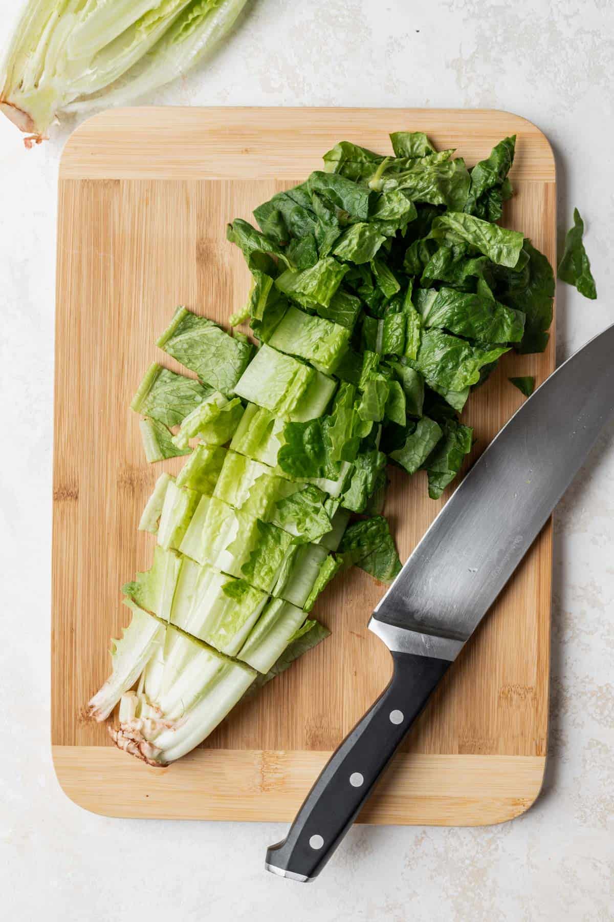 Romaine lettuce cut on a wooden cutting board with a chef's knife next to it.
