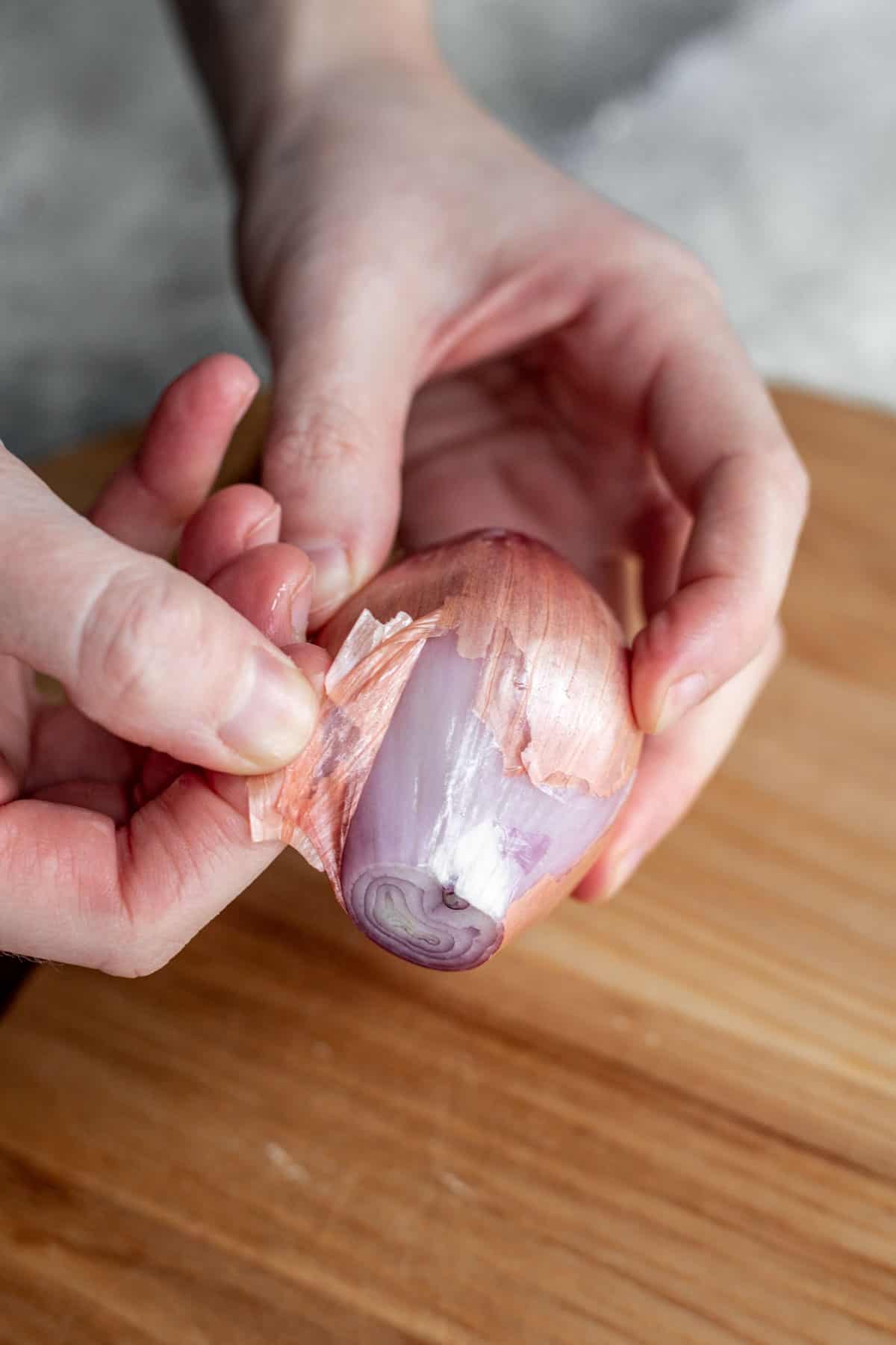 Two hands peeling the skin off a shallot.