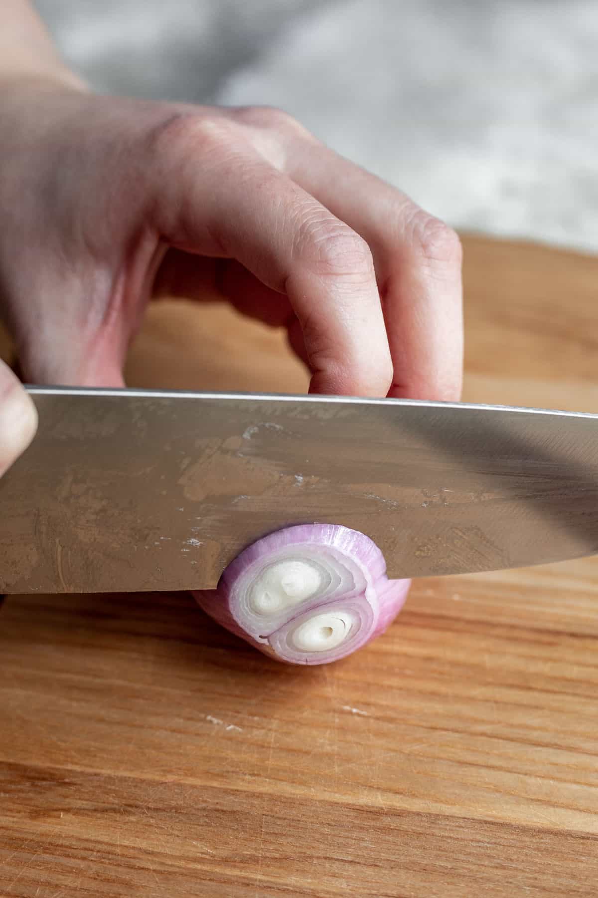 A chef's knife slicing a shallot into rings.