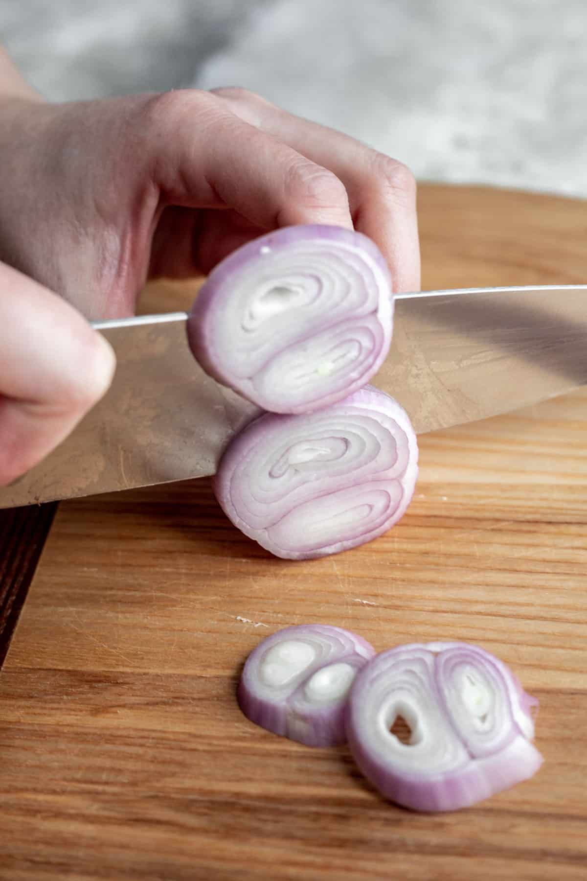 A chef's knife slicing a shallot into multiple rings.