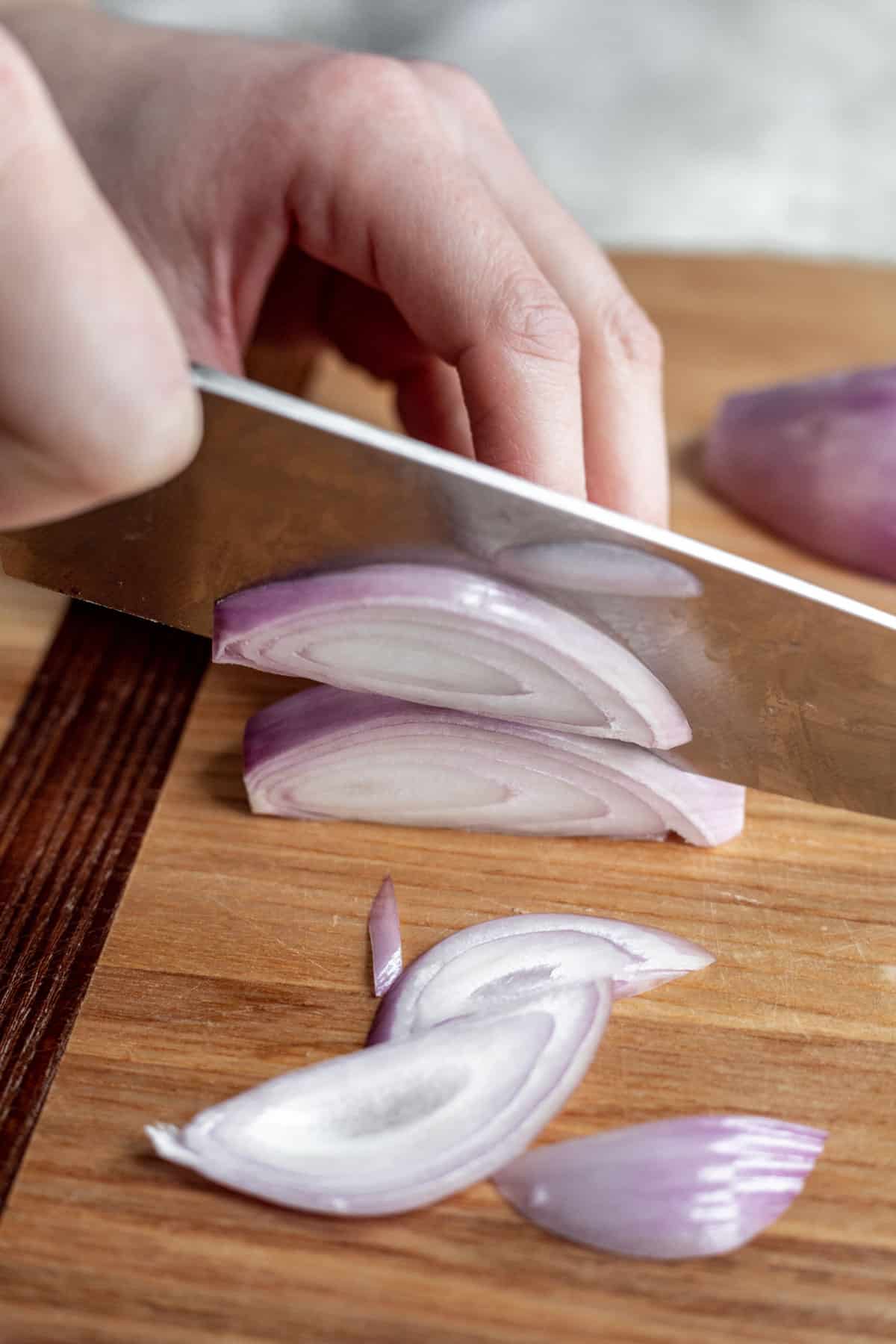 A chef's knife cutting a shallot into strips.