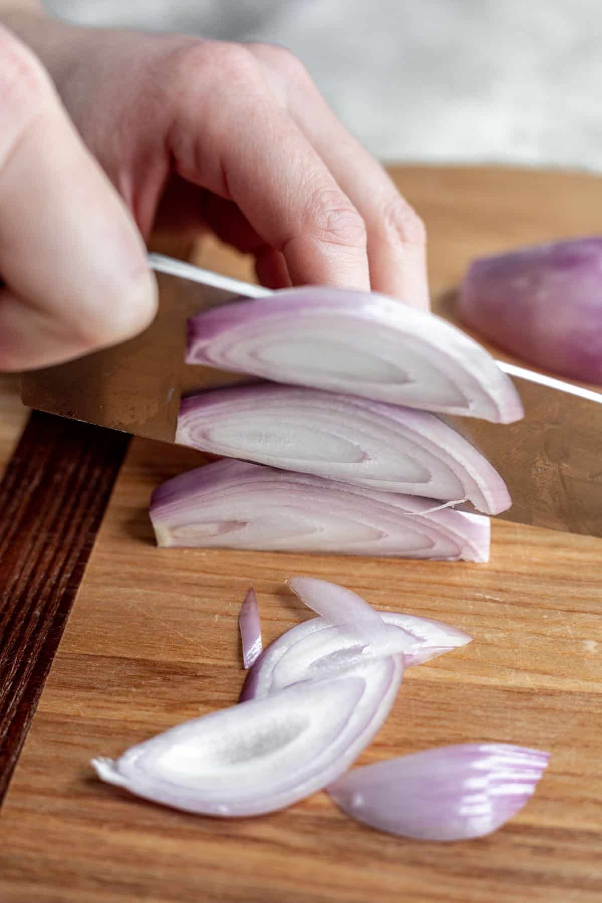 A chef's knife making multiple julienne slices into a shallot.