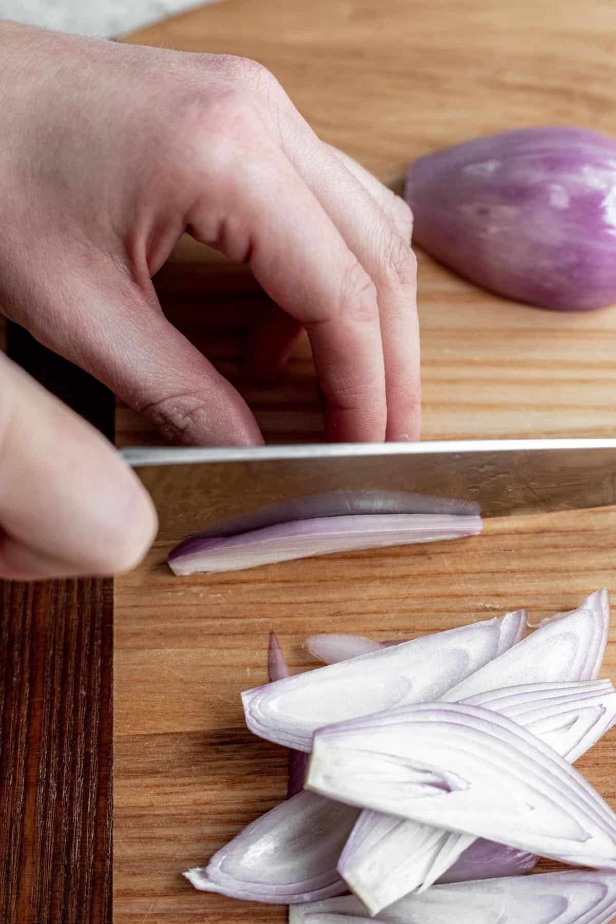 A chef's knife cutting a shallot into julienned strips.