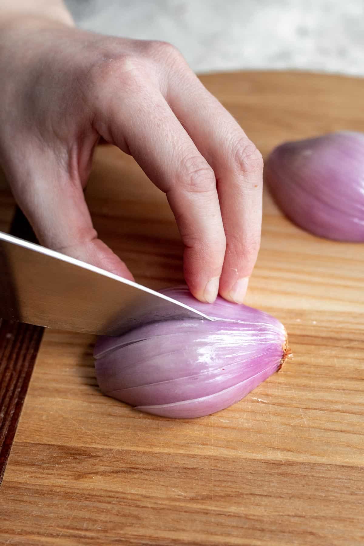 A chef's knife slicing a shallot without cutting through the shallot's root end.