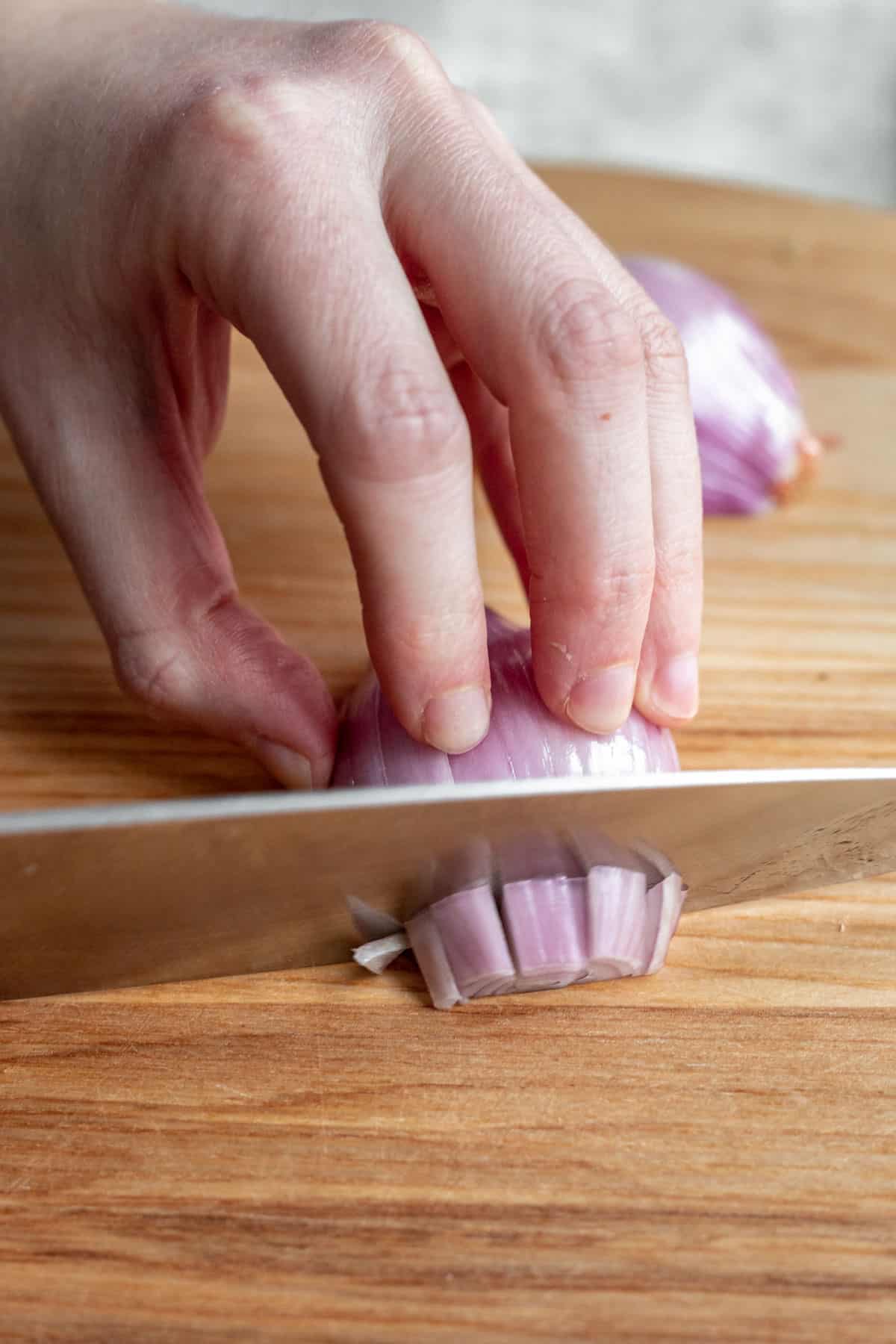 A chef's knife cutting the shallot the opposite way to dice it.
