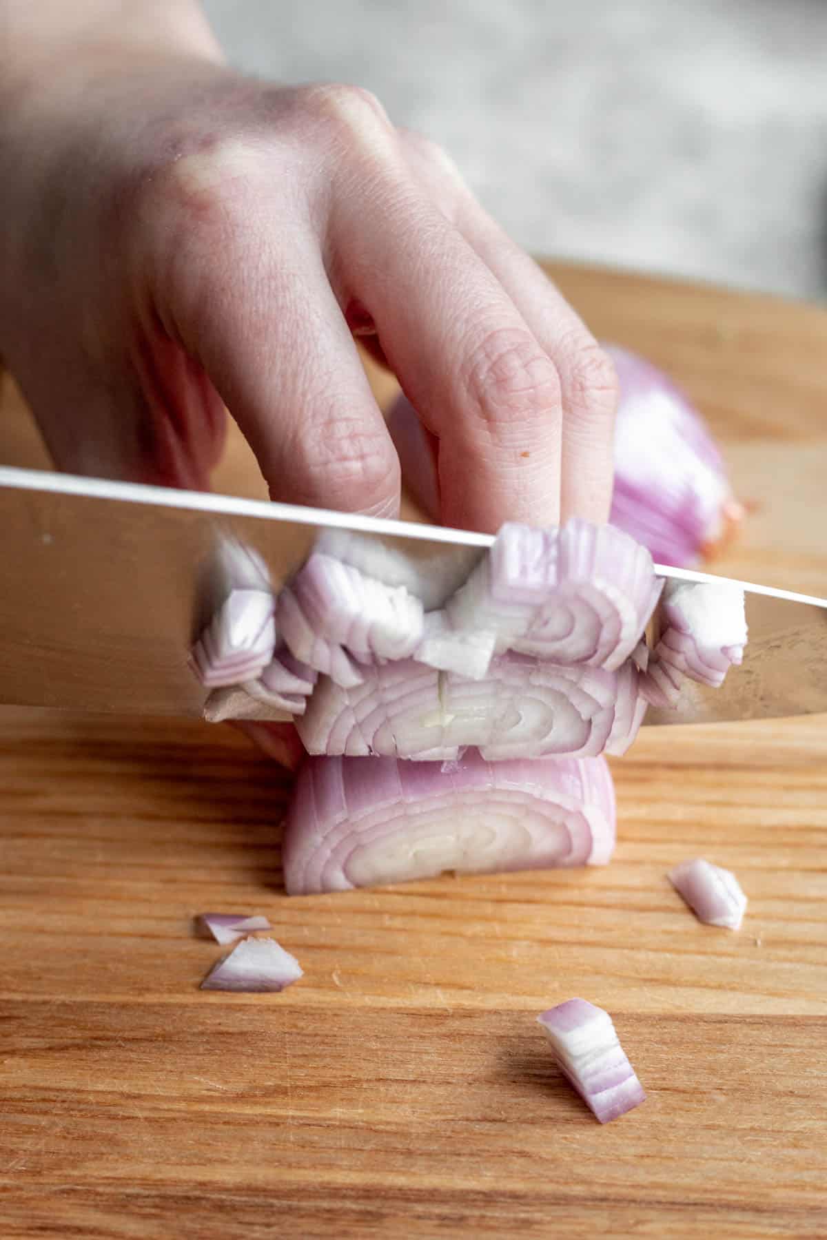 A chef's knife chopping a shallot on a cutting board.