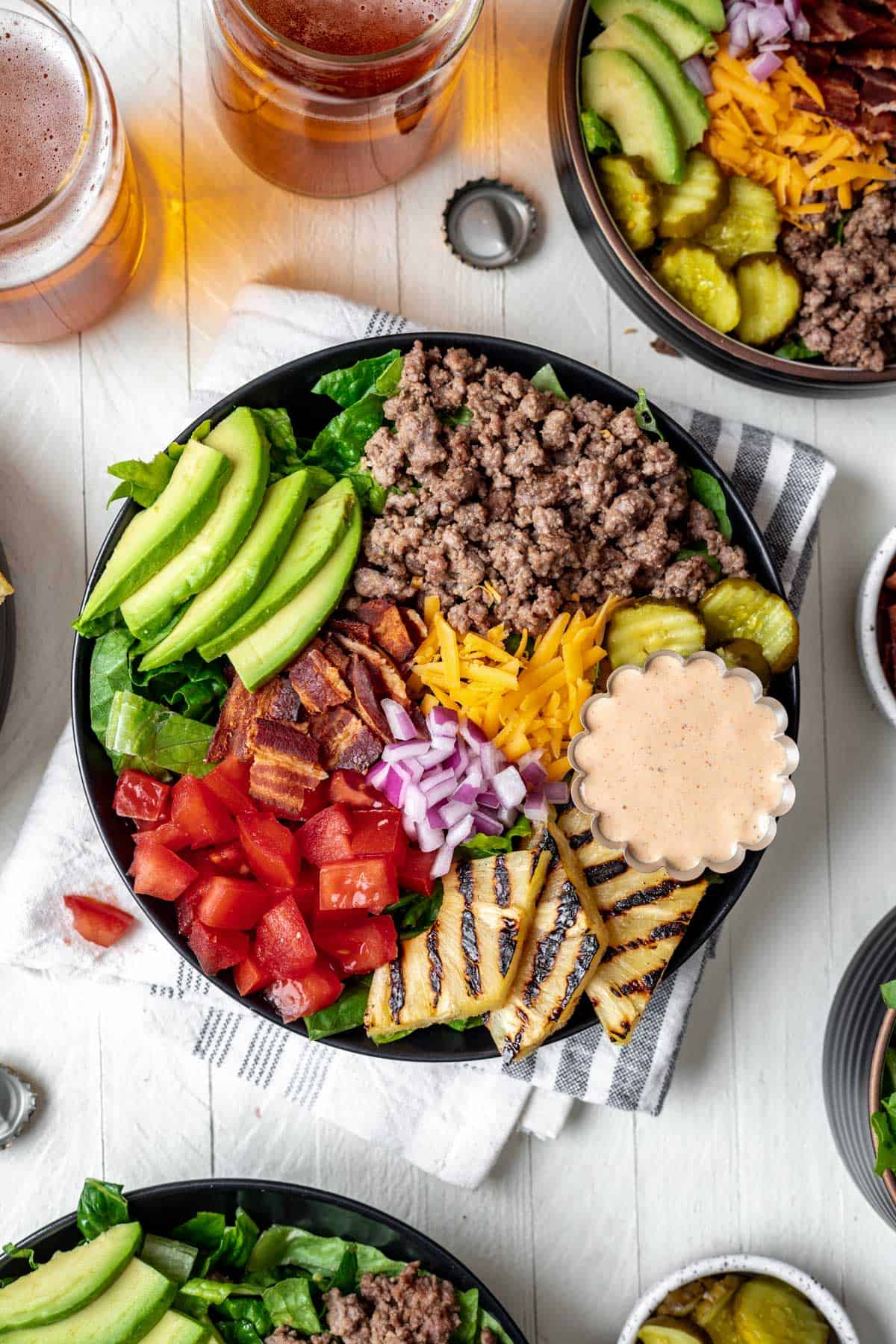 Loaded burger bowls topped with avocado, grilled pineapple, pickles, cheese, bacon, and tomatoes.