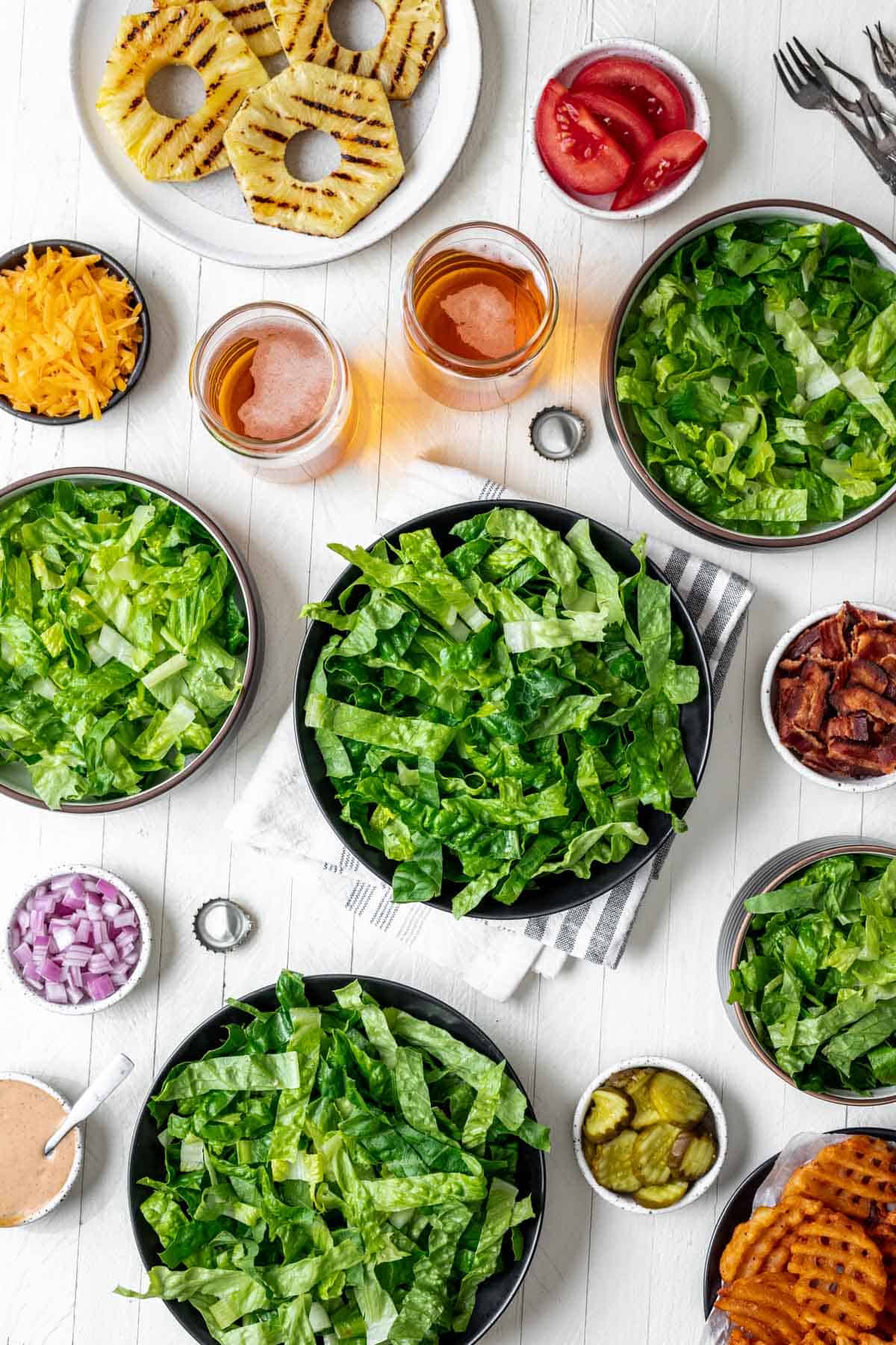 Bowls filled with lettuce surrounded by the rest of the burger fixings.