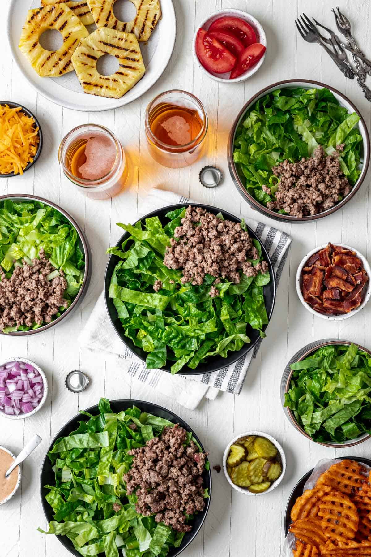 Bowls filled with lettuce and ground beef surrounded by the rest of the burger fixings.