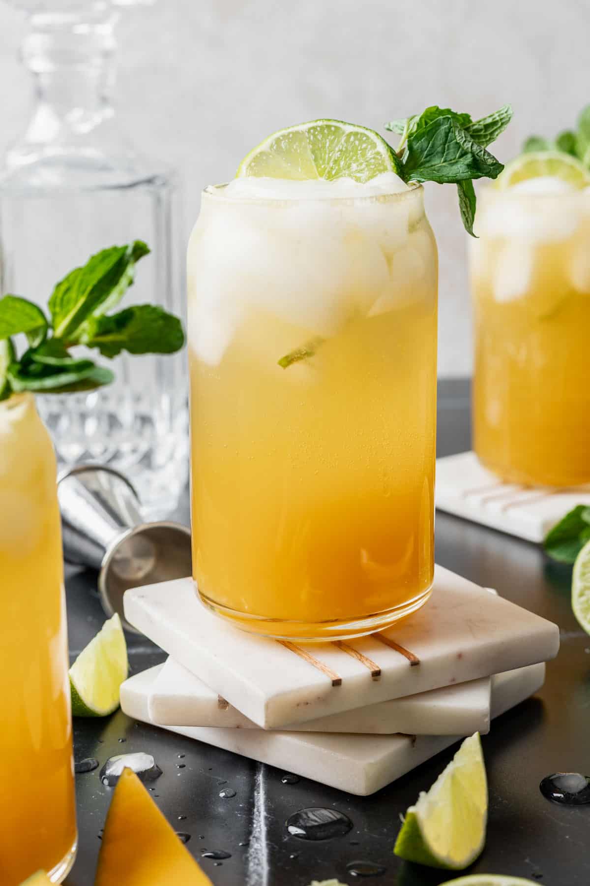 Mango mojito garnished with a lime slice and mint on top of white coasters.