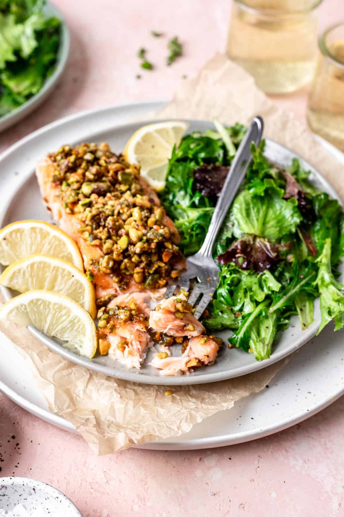 Pistachio crusted salmon on a plate with a side salad and a fork.