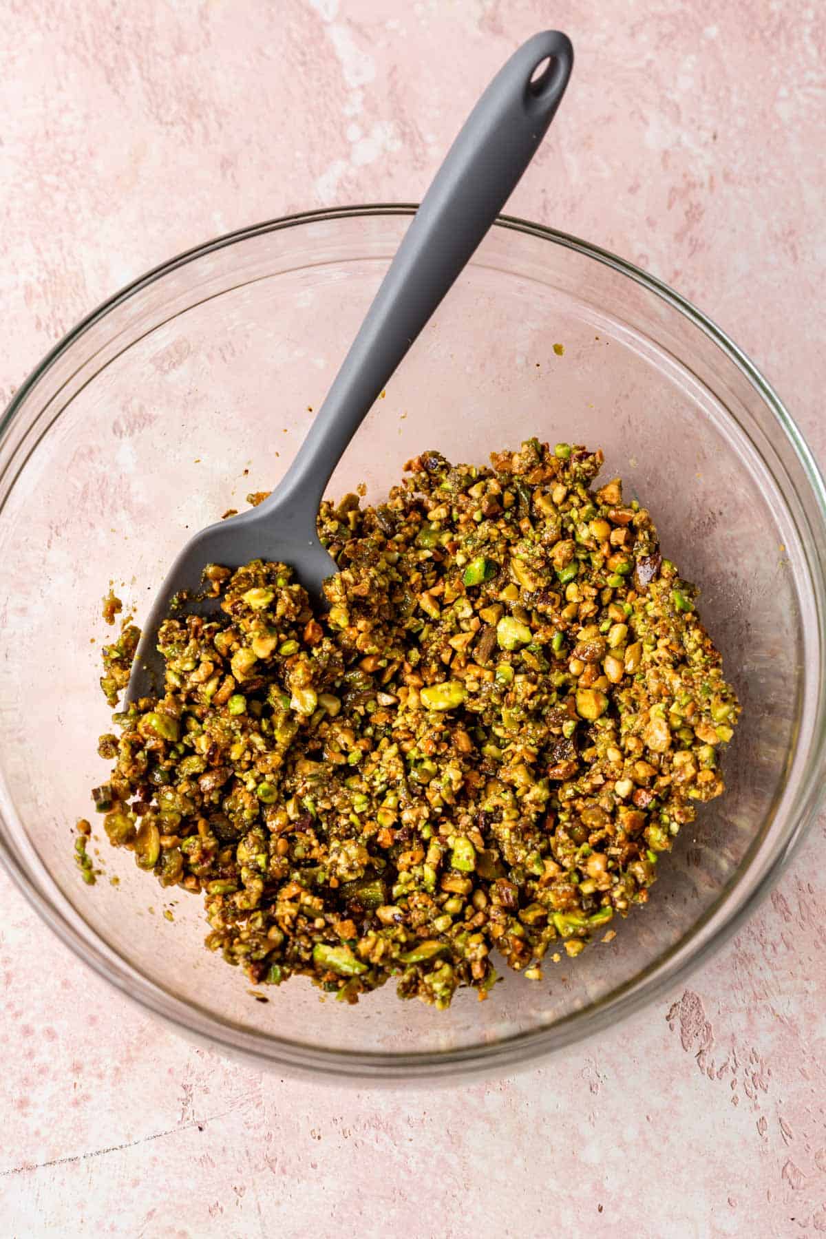 Pistachios combined with olive oil and dijon in a glass mixing bowl.