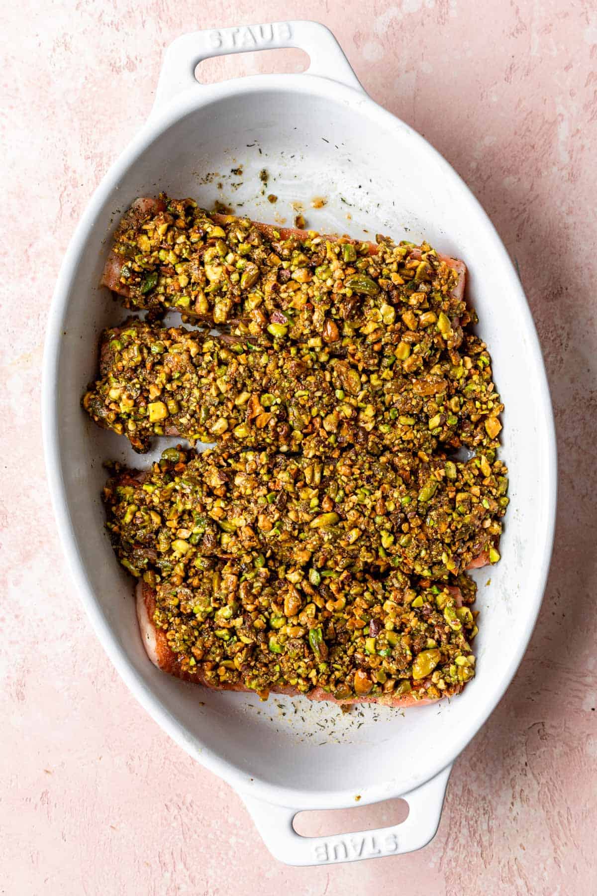 4 filets of salmon topped with crushed pistachios in a baking dish.