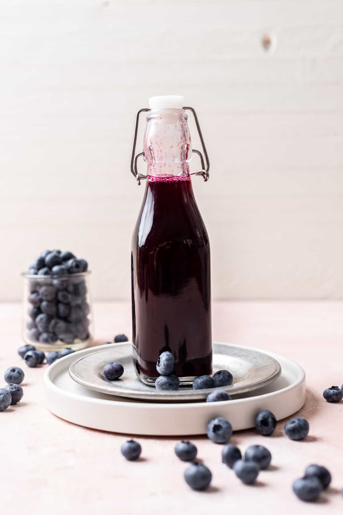 Blueberry simple syrup in a glass bottle surrounded by fresh blueberries.