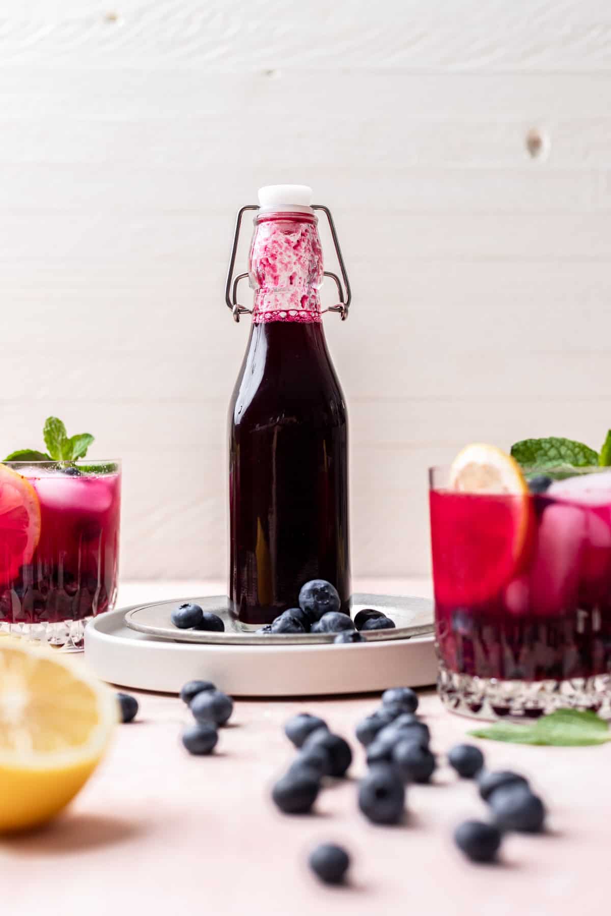 Blueberry simple syrup in a glass bottle with fresh blueberries around it.