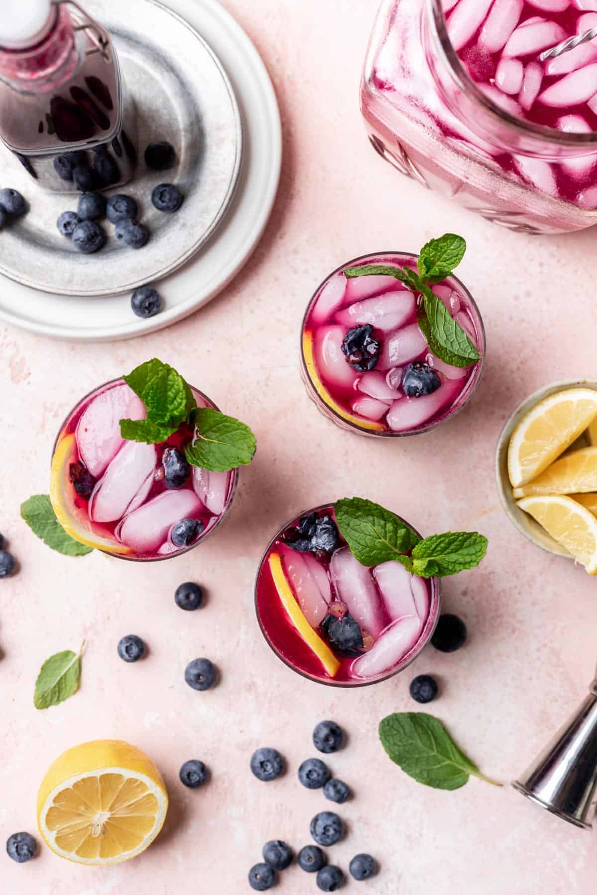 3 glasses of blueberry vodka lemonade with blueberries around them.