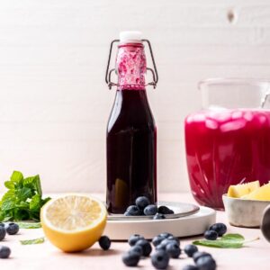 Blueberry simple syrup in a glass bottle with lemon and blueberries around it.