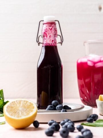 Blueberry simple syrup in a glass bottle with lemon and blueberries around it.