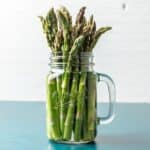 A bunch of asparagus in a glass jar with water.