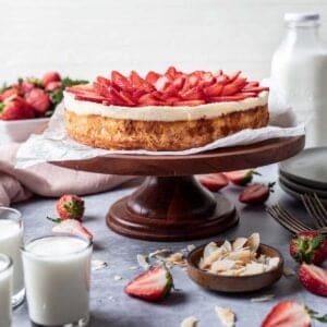 Kosher for passover cheesecake on a cake stand with toasted coconut and strawberries around it.