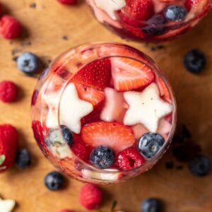 Red, white, and blue sangria in a wine glass filled with berries and star-shaped fruits.