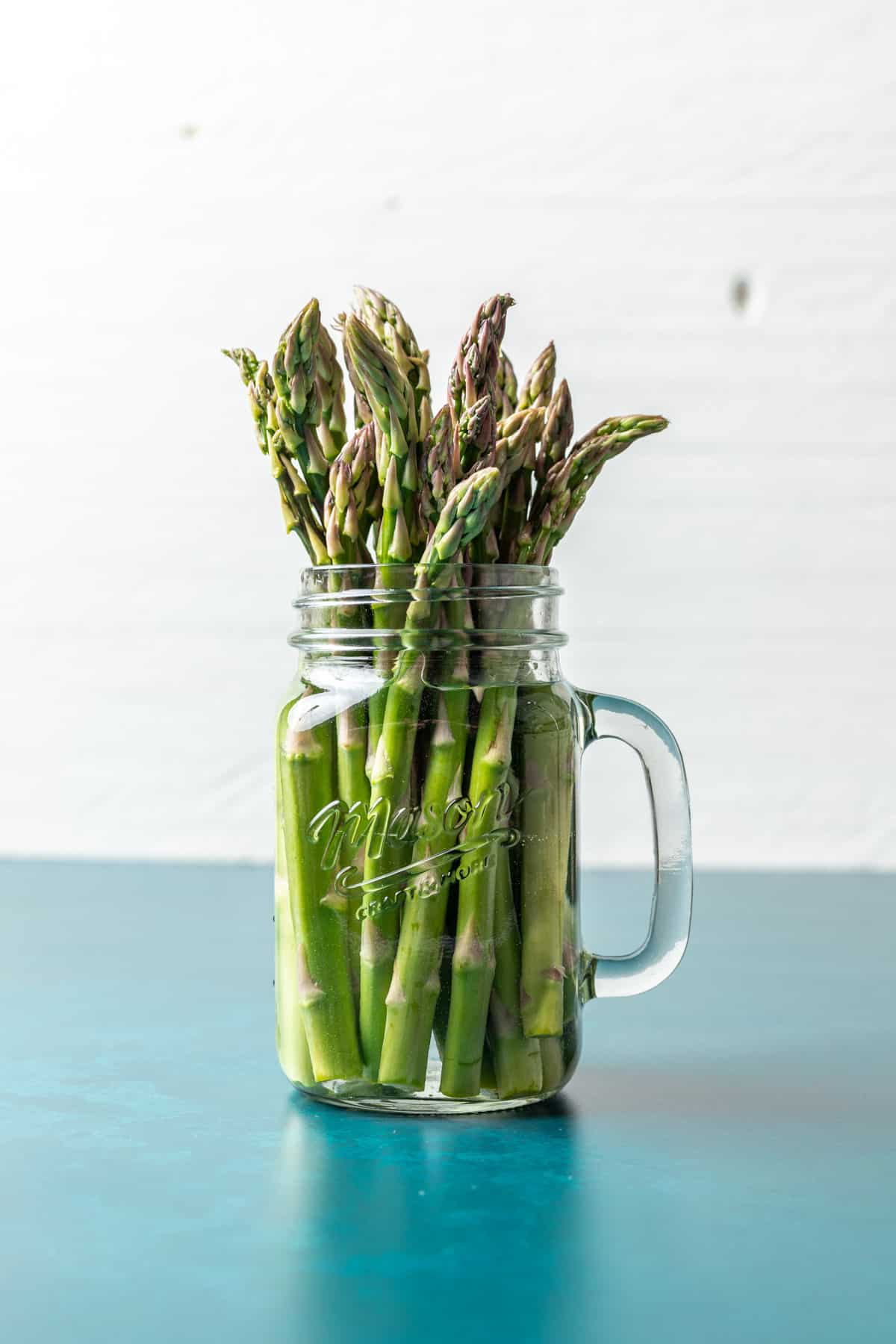 A bunch of asparagus in a glass jar with water.