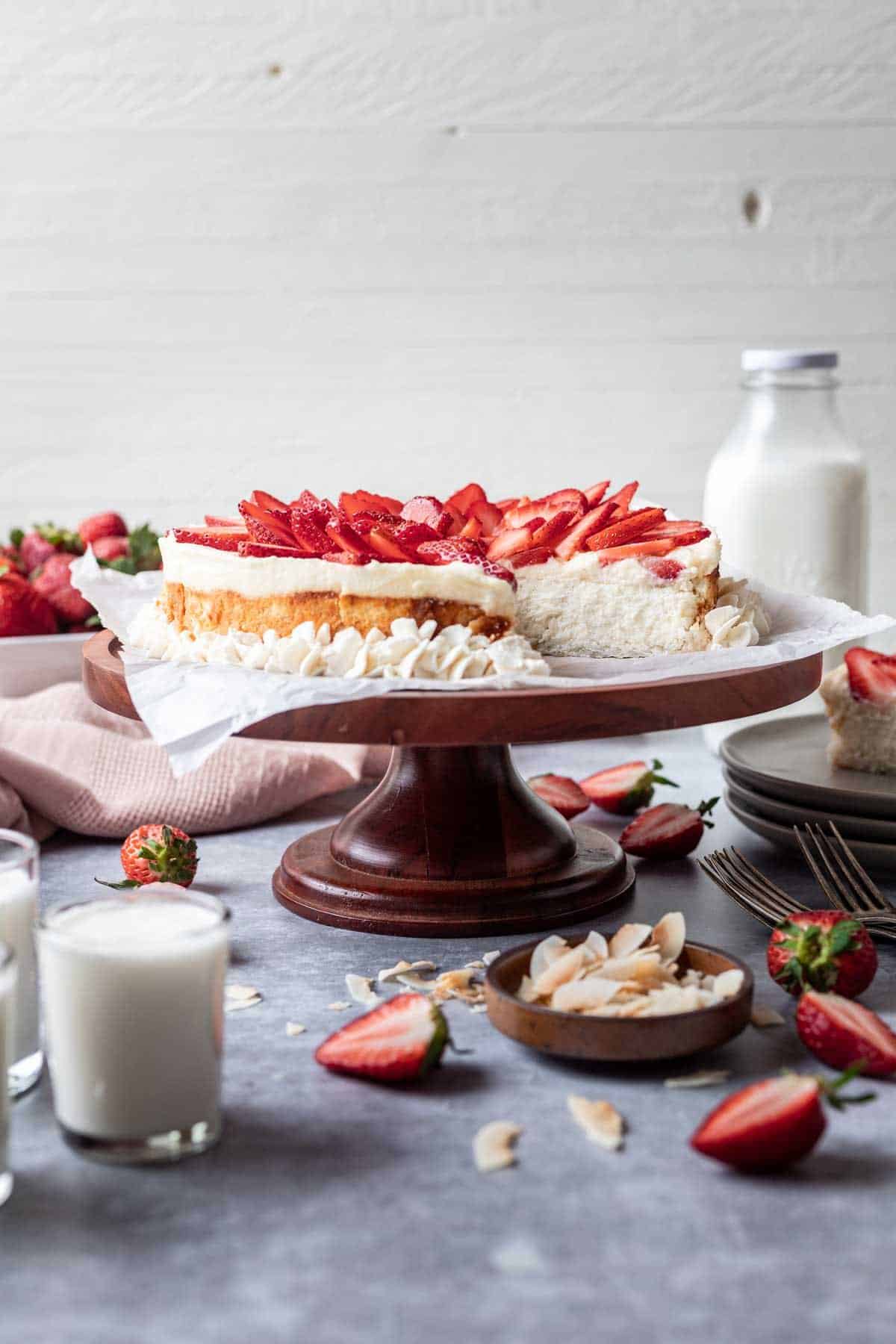 Kosher for passover cheesecake on a cake stand with toasted coconut and strawberries around it.