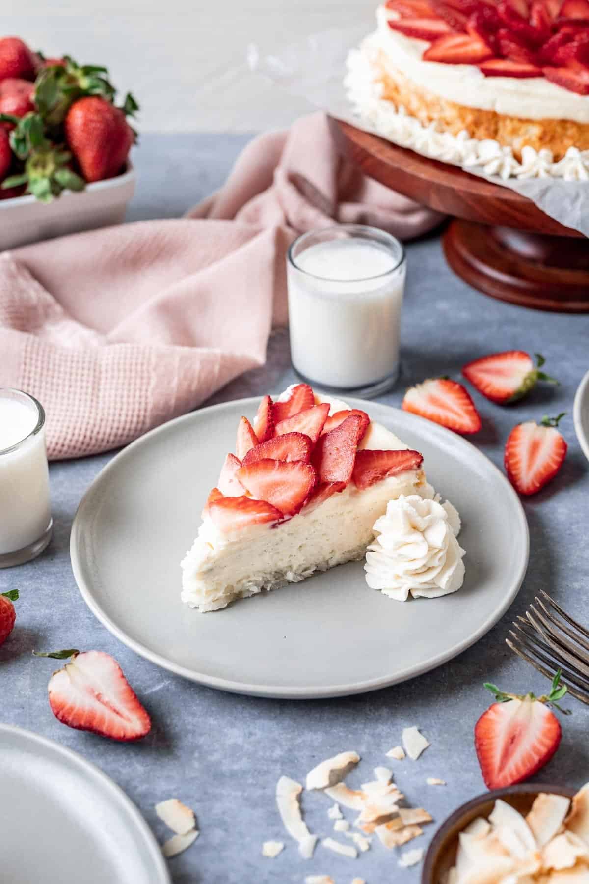A slice of vanilla bean kosher for passover cheesecake on a gray plate with whipped cream and sliced strawberries.