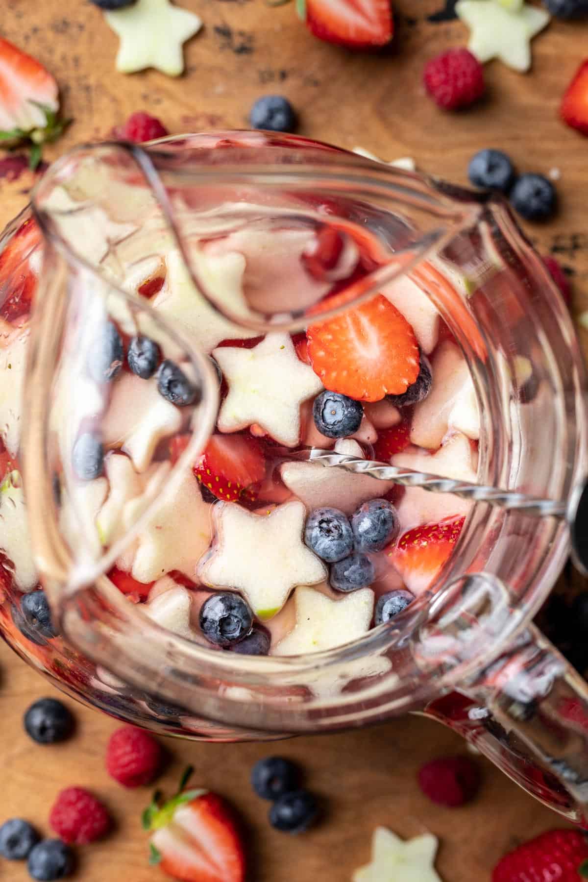 Red, white, and blue sangria with berries and star-shaped fruit in a pitcher.