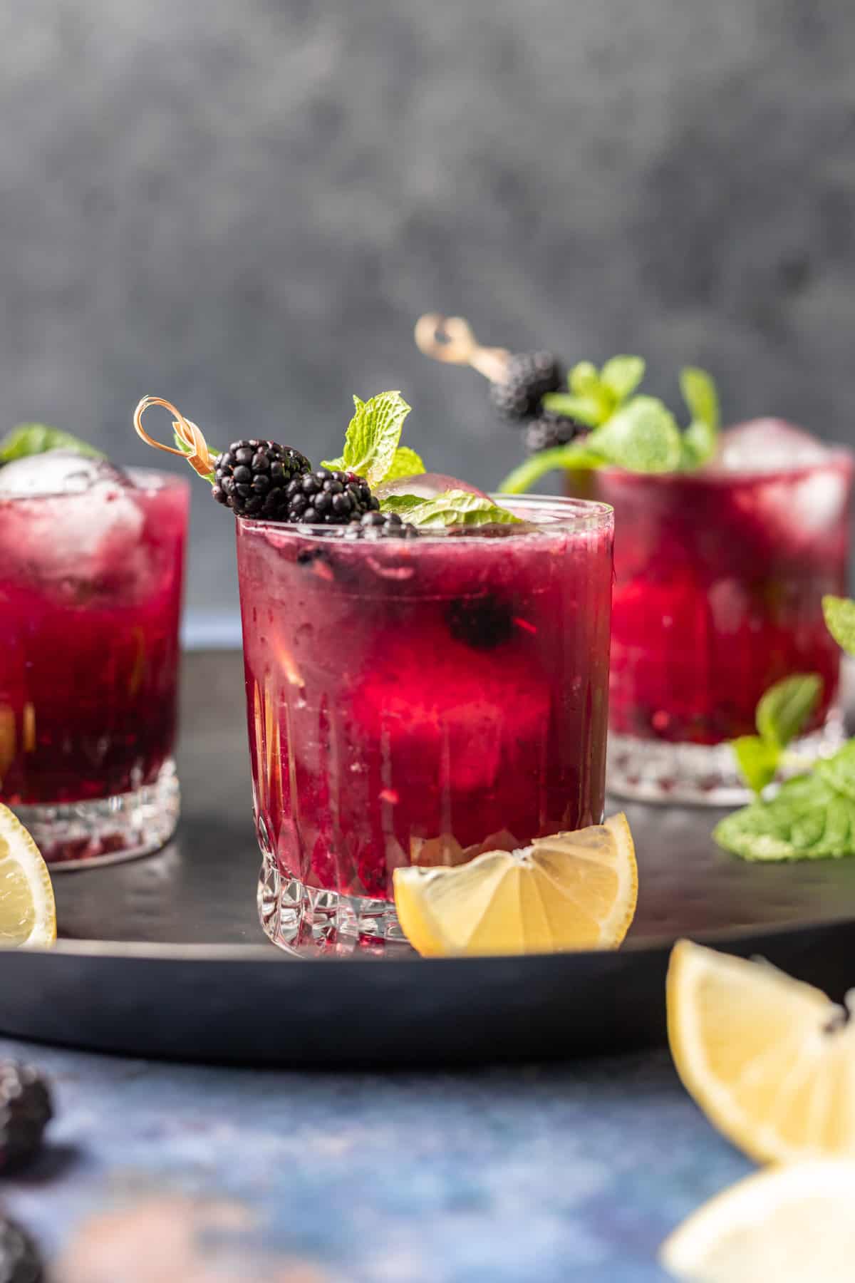 Blackberry bourbon smash on a serving tray with lemon wedges.