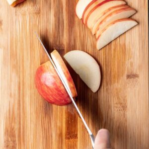 Slicing an apple on a wooden cutting board with a sharp chef's knife.