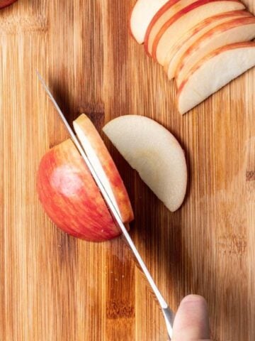 Slicing an apple on a wooden cutting board with a sharp chef's knife.