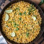 Skillet roasted corn kernels in a cast iron skillet with parsley and lime wedges.