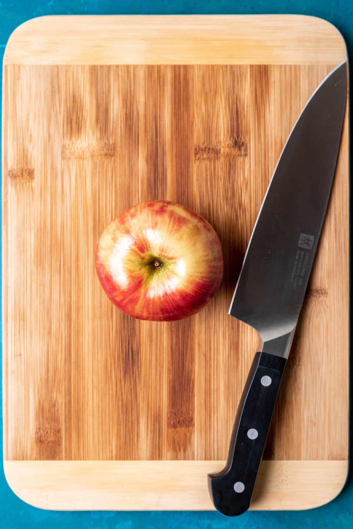 An apple on a cutting board with a chef's knife.