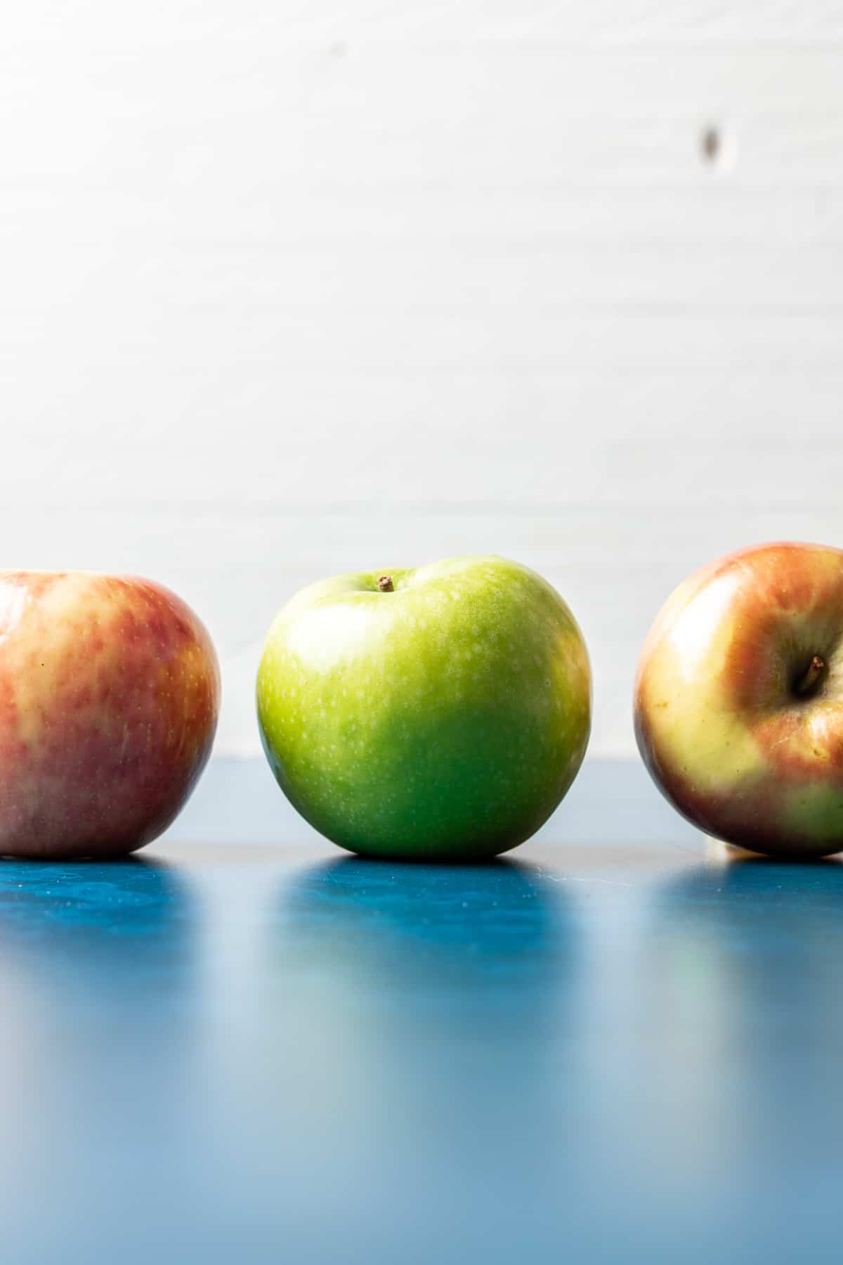 2 red apples and 1 green apple on a blue surface.