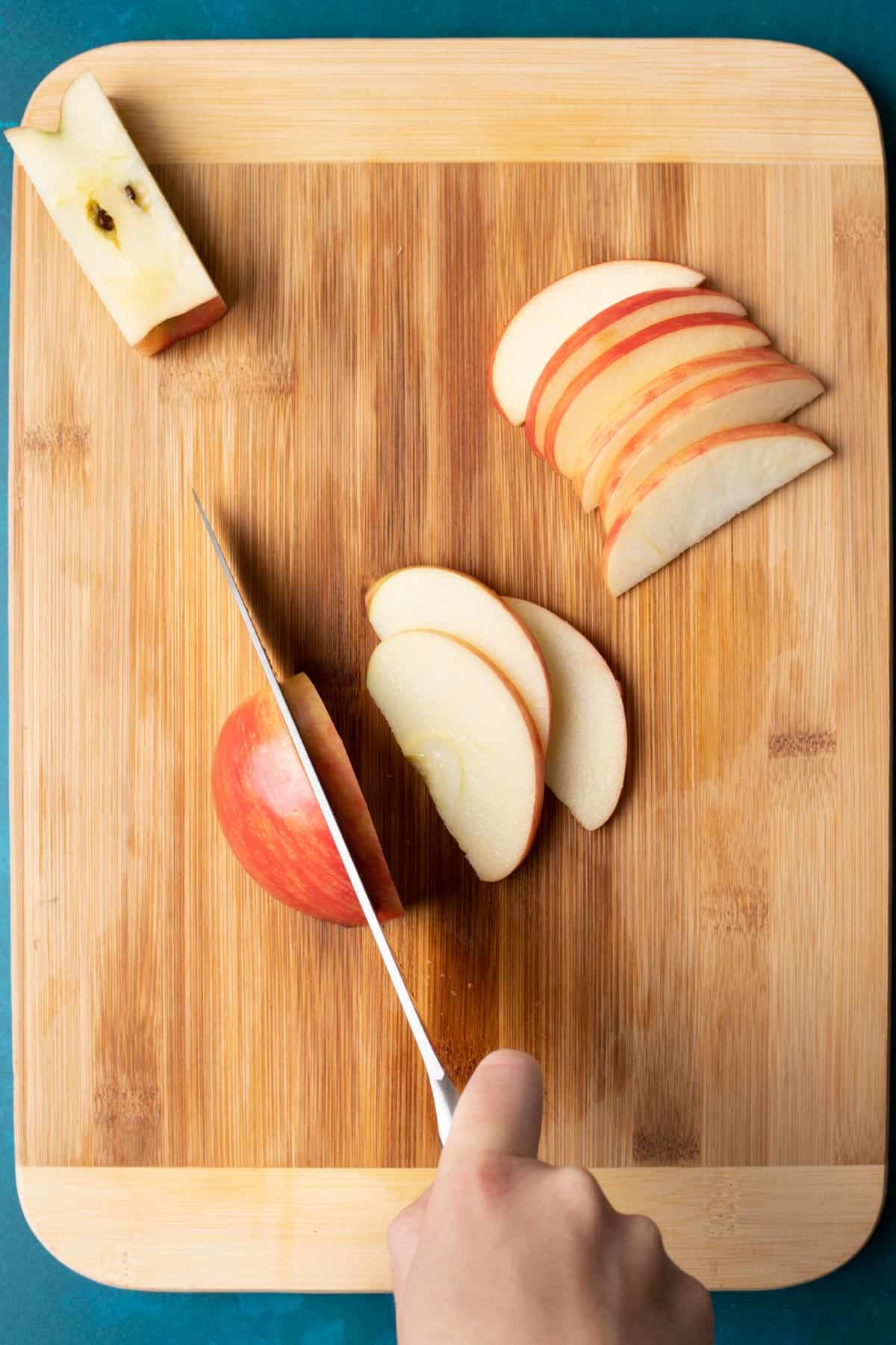 A knife cutting the sides of an apple into thin slices.