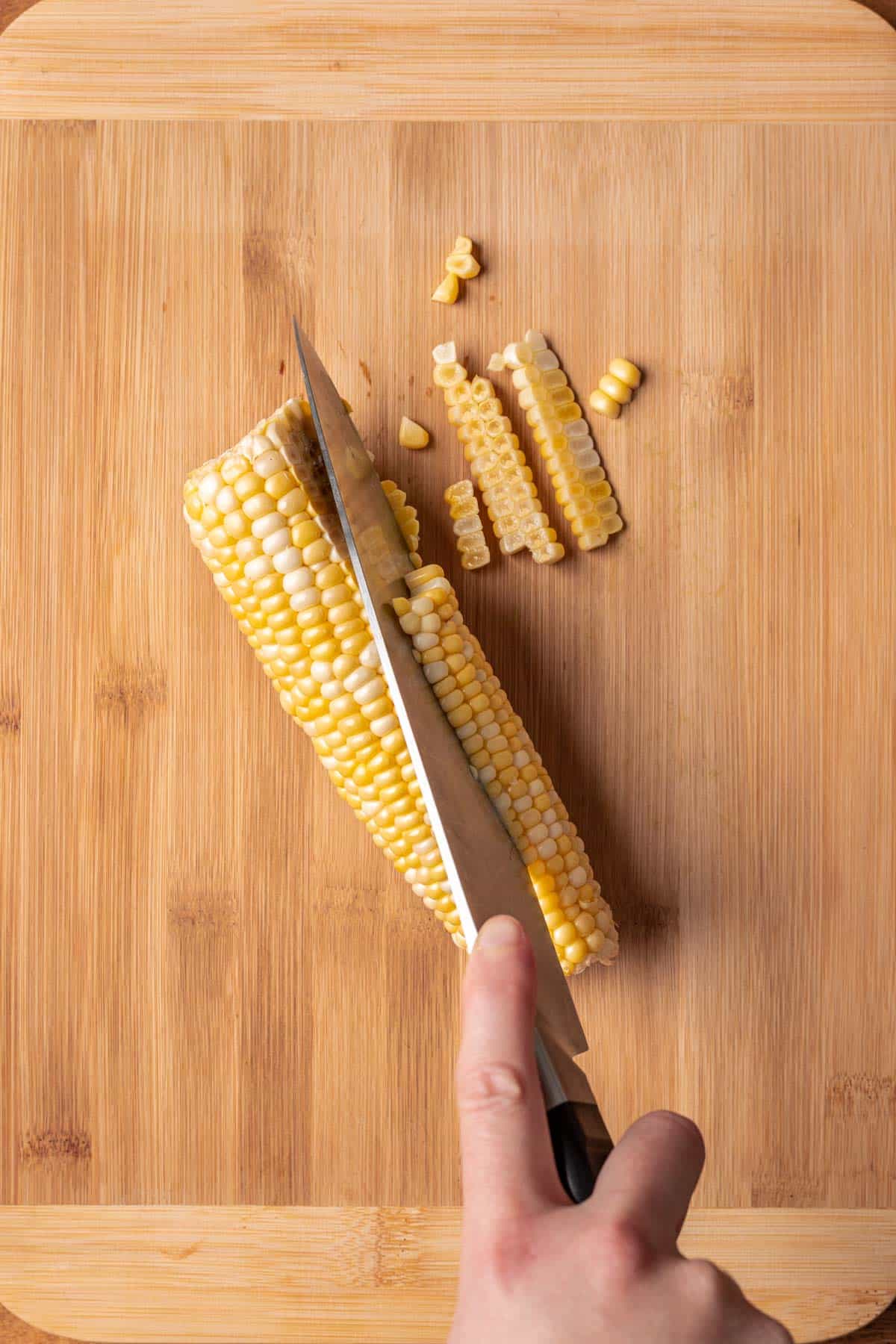 A chef's knife cutting corn off the side of the cob.