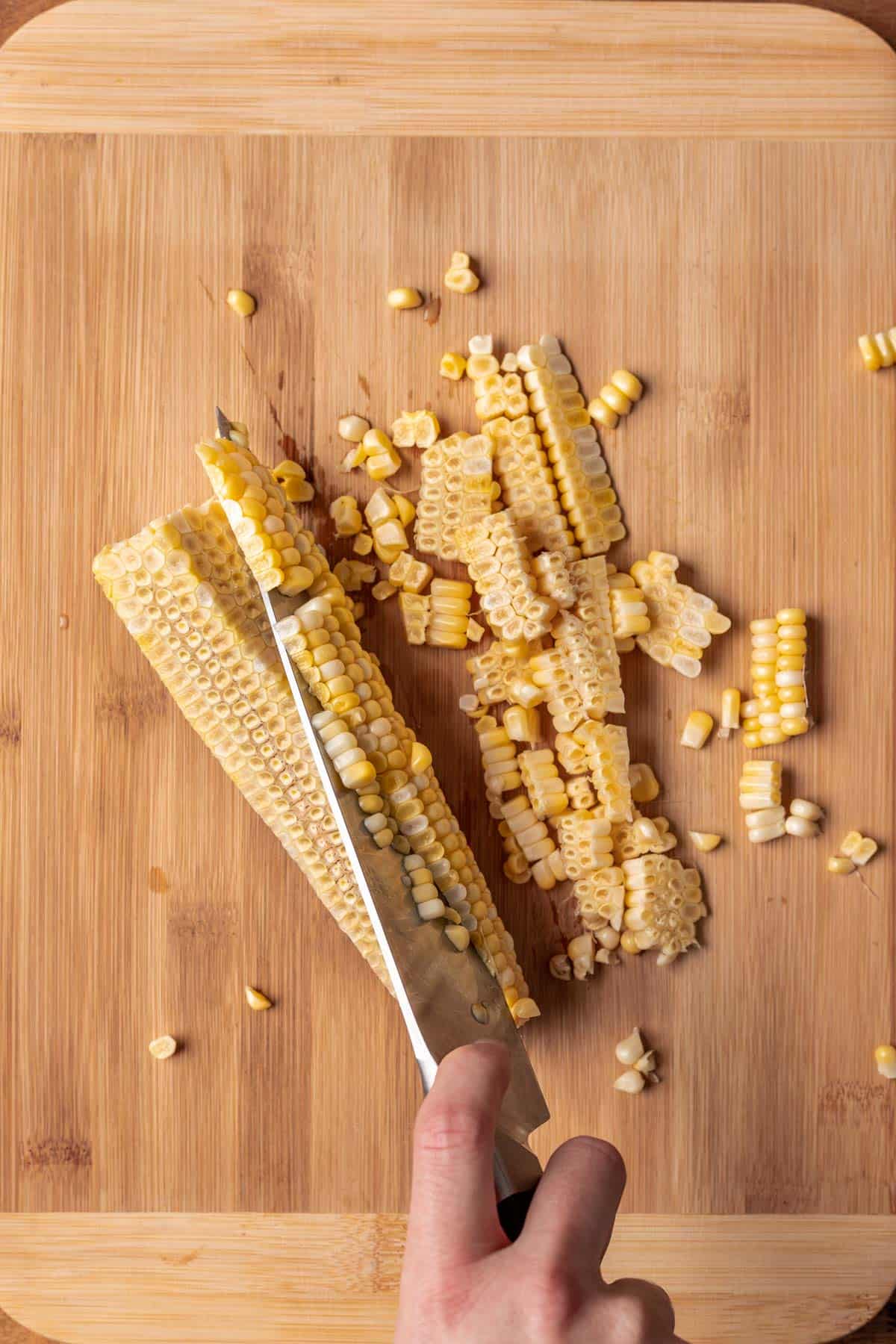 A chef's knife cutting the rest of the corn off the cob.